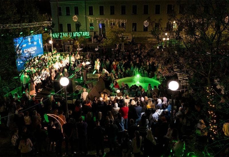 Manifestacija Ramazan u Mostaru noću: publika ispred pozornice i osvijetljene fontane, natpis Ramazan u Mostaru